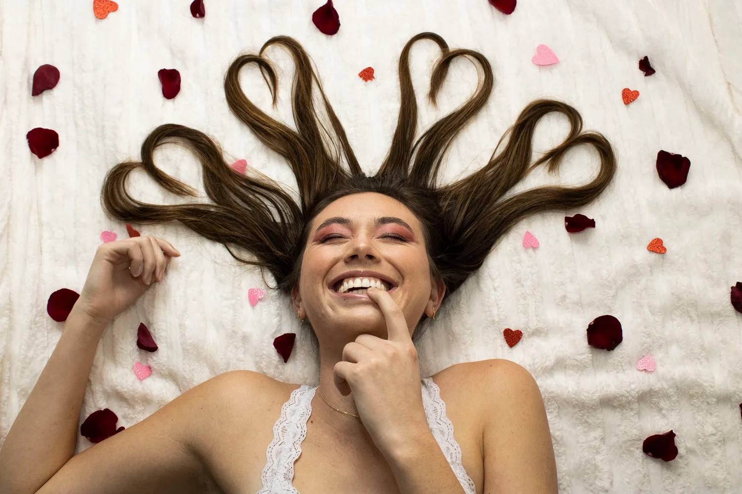 Laughing young woman lying on a bed with her hair shaped into hearts and rose petals