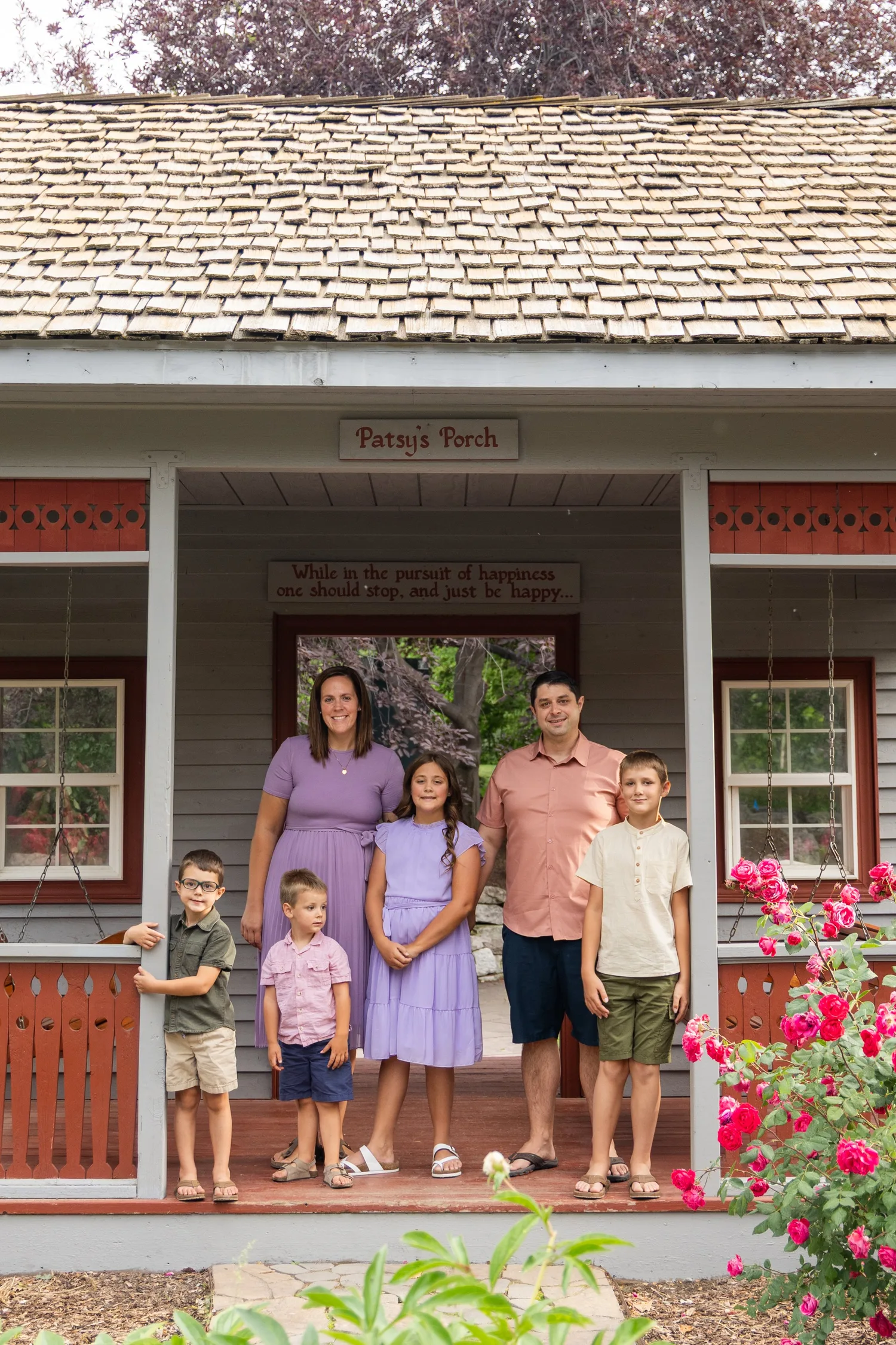 Family of six on the porch of a red-trimmed cottage with roses
