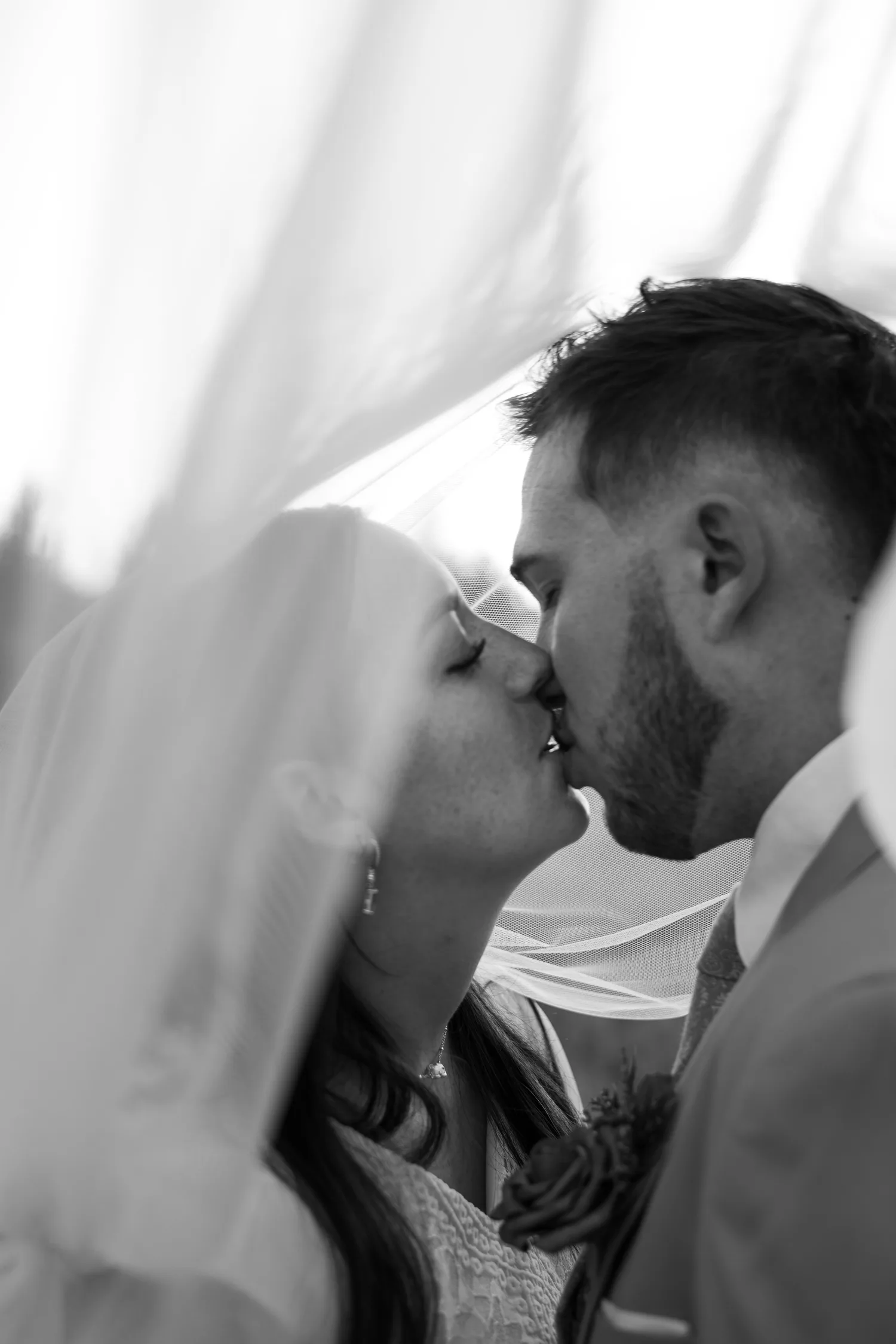 Black-and-white close-up of a bride and groom kissing under her veil