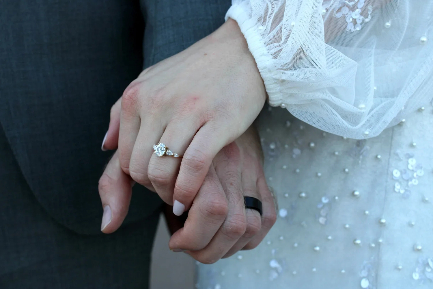 Close-up of the bride's diamond ring and the groom's black band as they hold hands