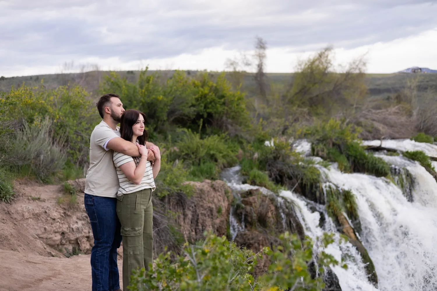 Couple embracing beside a waterfall overlooking a wide valley