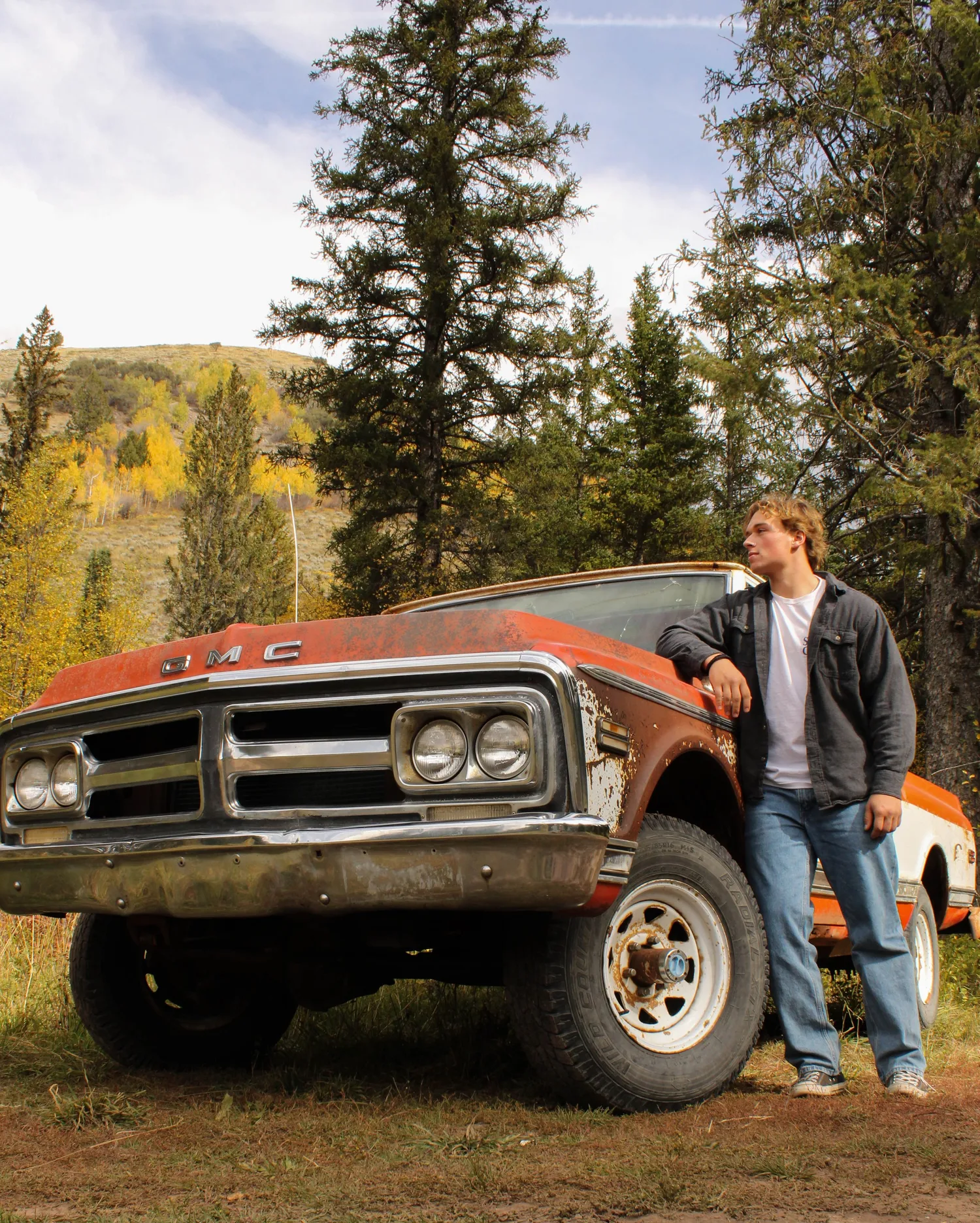 Senior portrait of a young man leaning on a vintage rusty GMC truck in the mountains