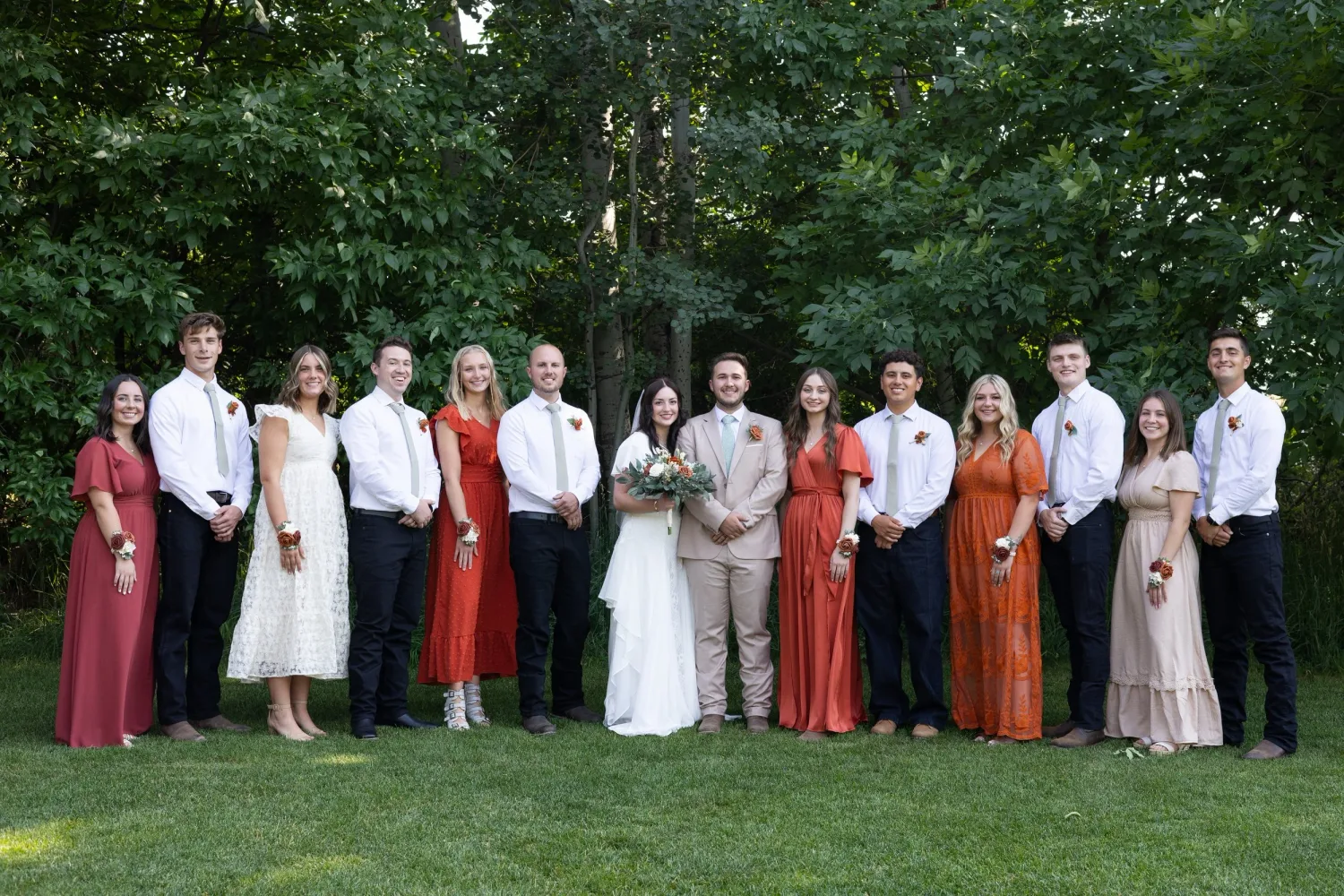 Full wedding party with bridesmaids in autumn-toned dresses and groomsmen on a lawn