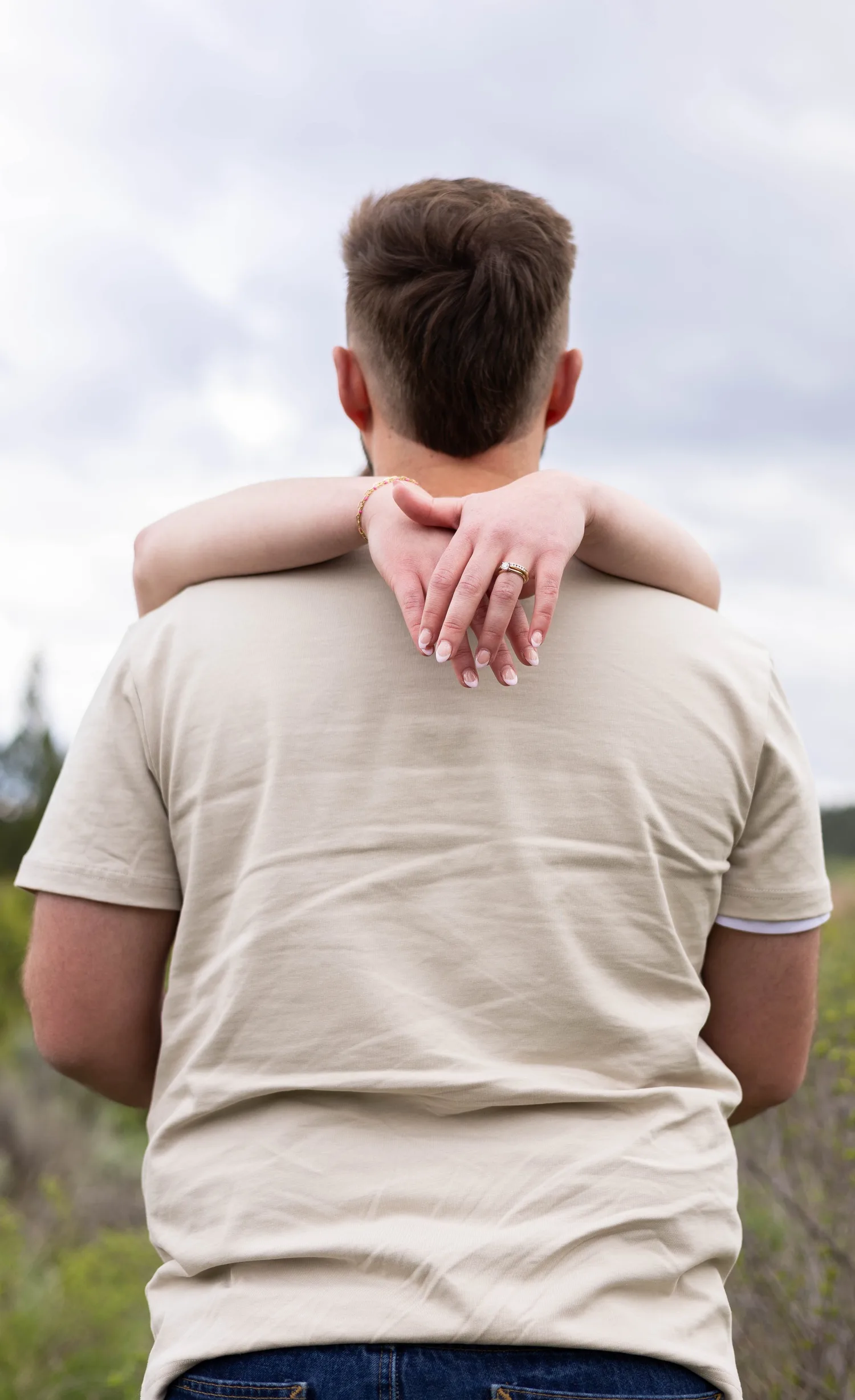 Woman's arms wrapped around her fiancé's neck, showing her engagement ring