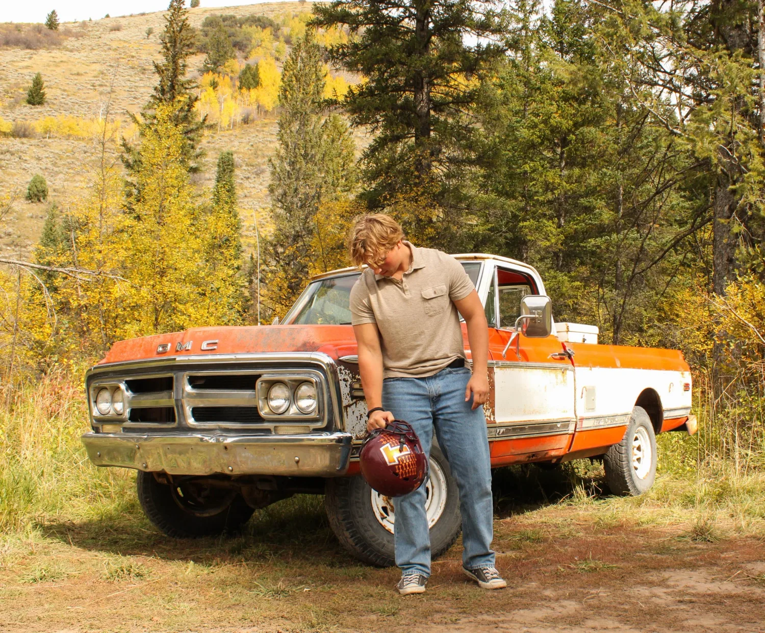 Senior football portrait of a young man with his helmet beside a vintage GMC truck