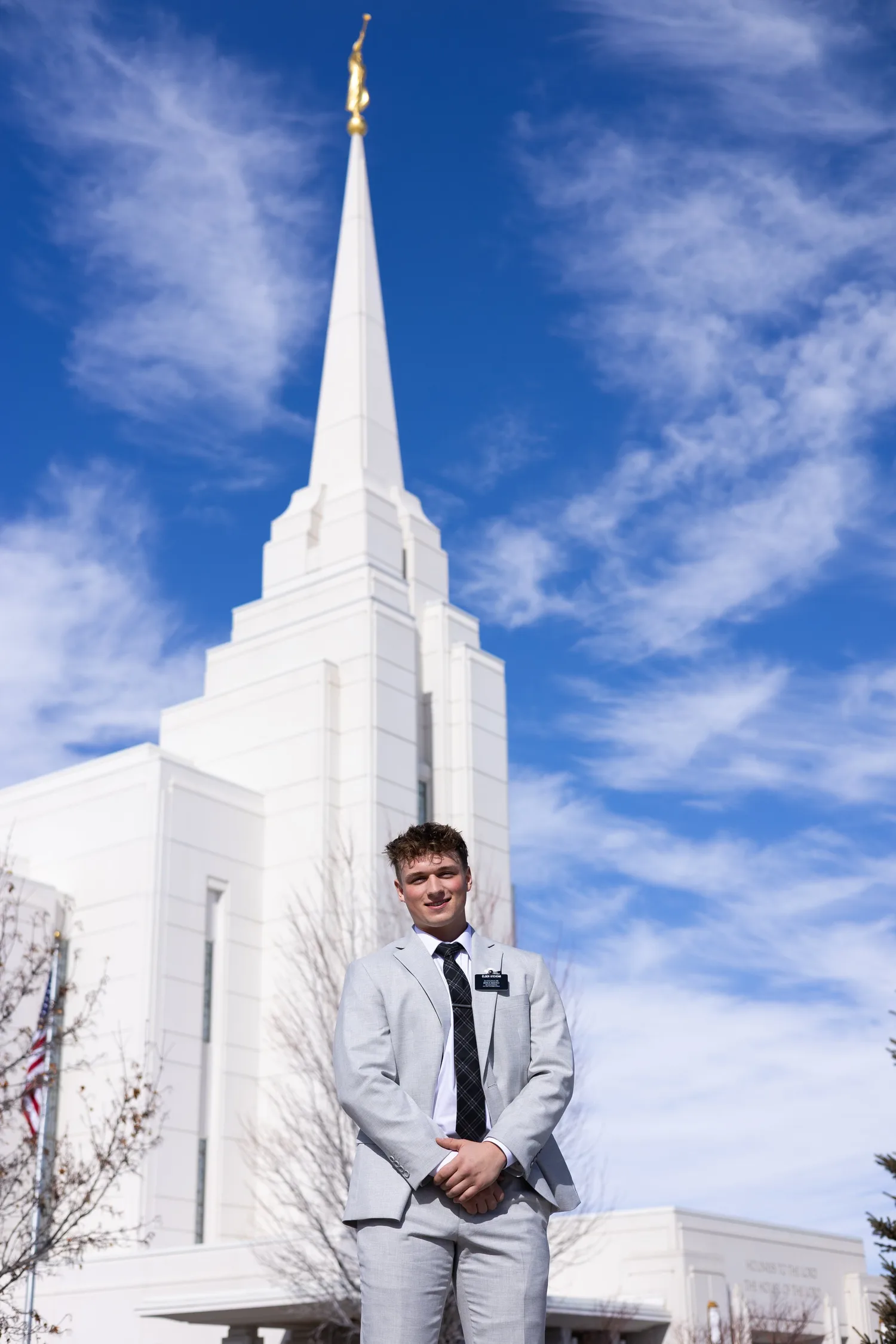 Missionary portrait in a gray suit in front of a white temple spire against a blue sky