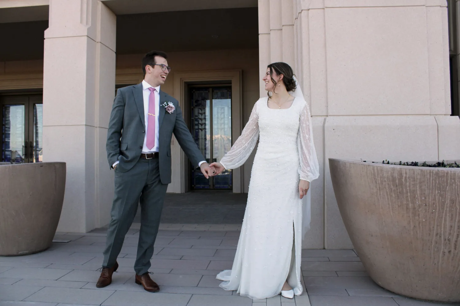 Bride and groom holding hands and laughing outside a temple entrance