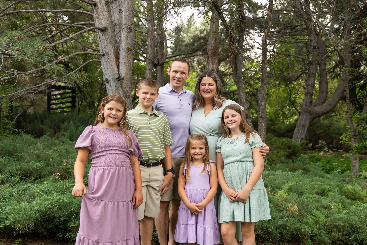 Parents and four children in lavender and sage outfits among trees
