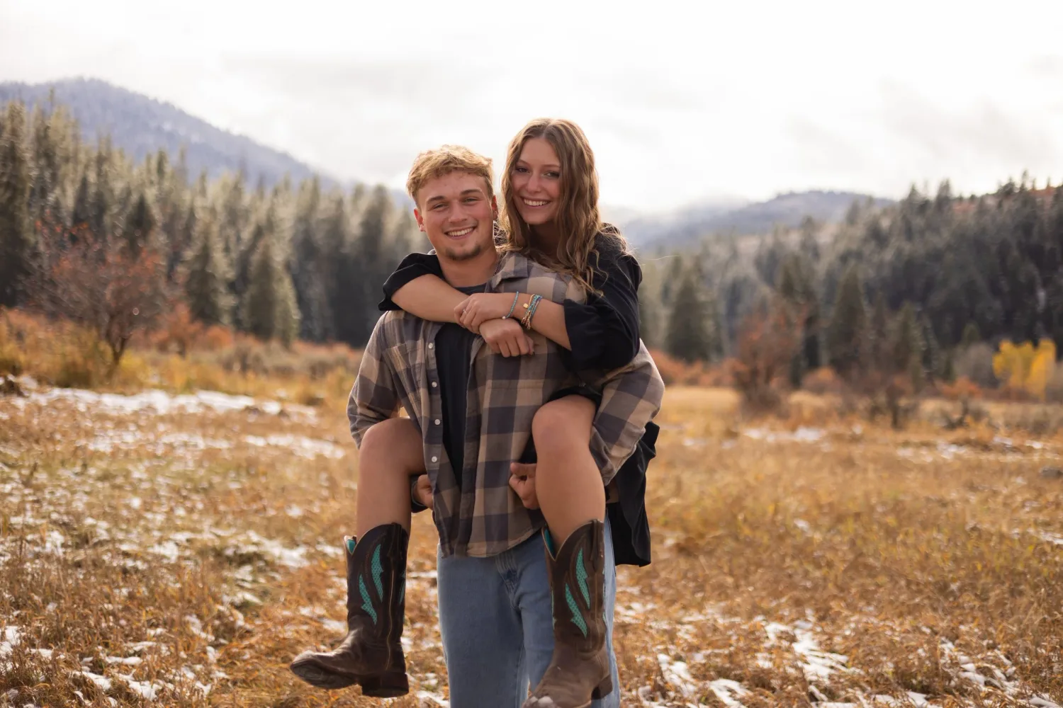 Man giving his girlfriend a piggyback ride in an autumn mountain meadow with light snow