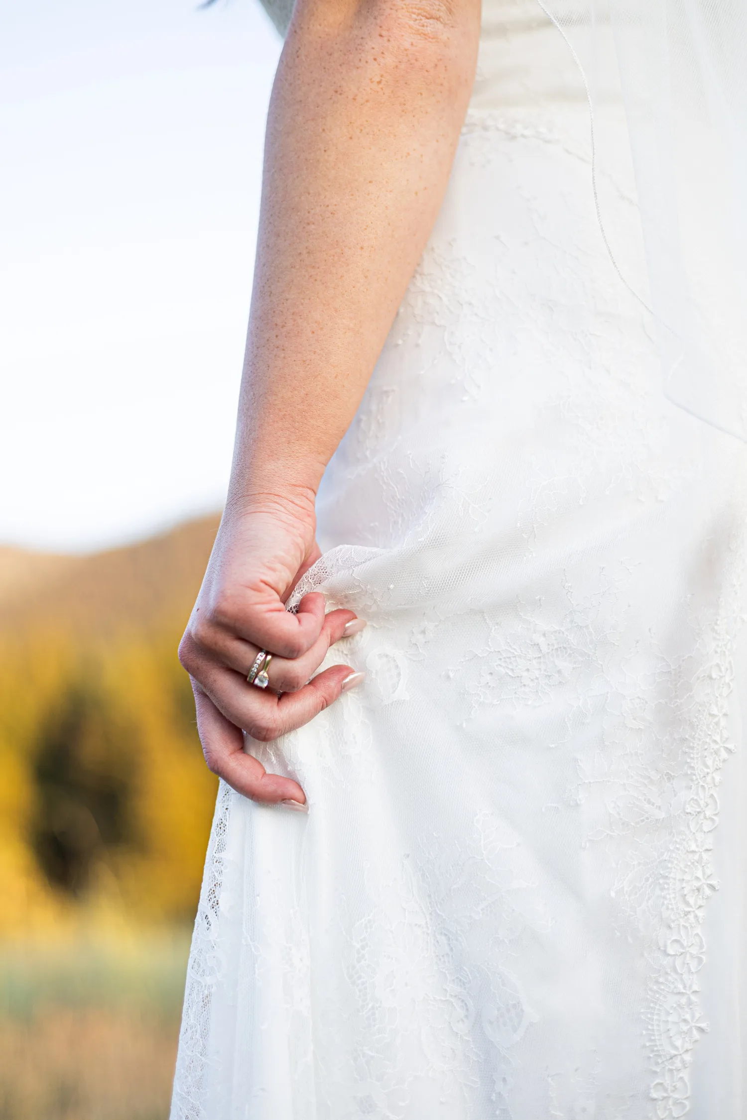 Close-up of a bride's hand with her engagement ring resting on her lace wedding dress
