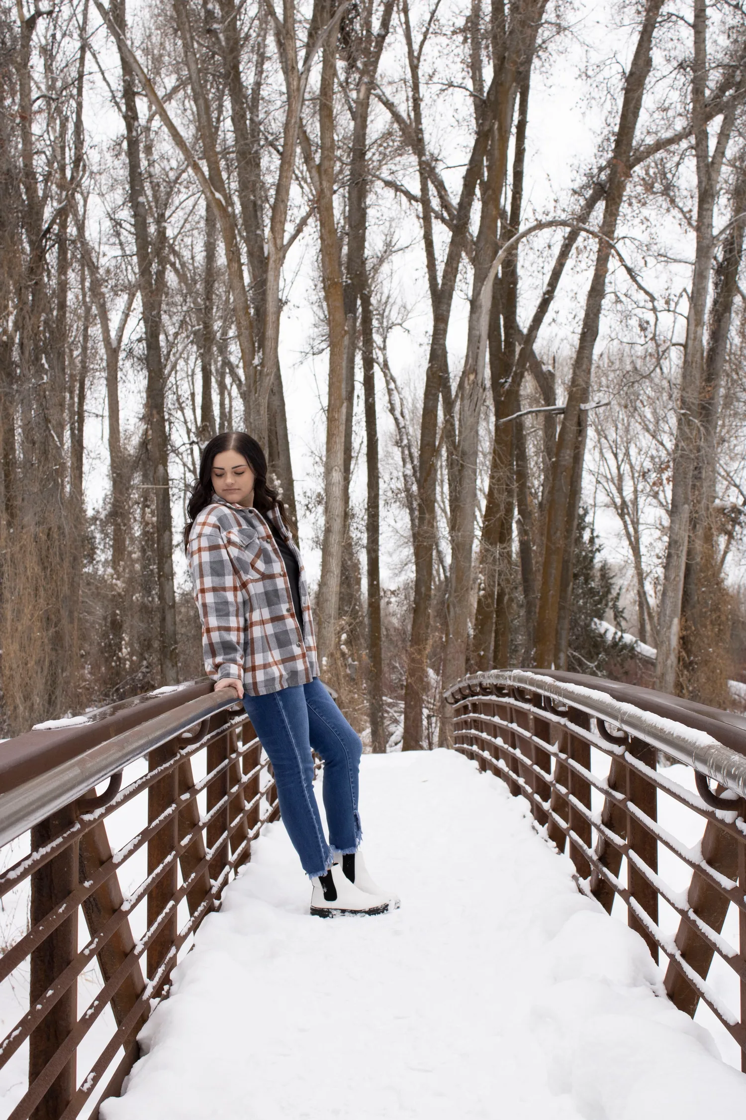 Young woman in a plaid jacket leaning on a snowy footbridge in winter