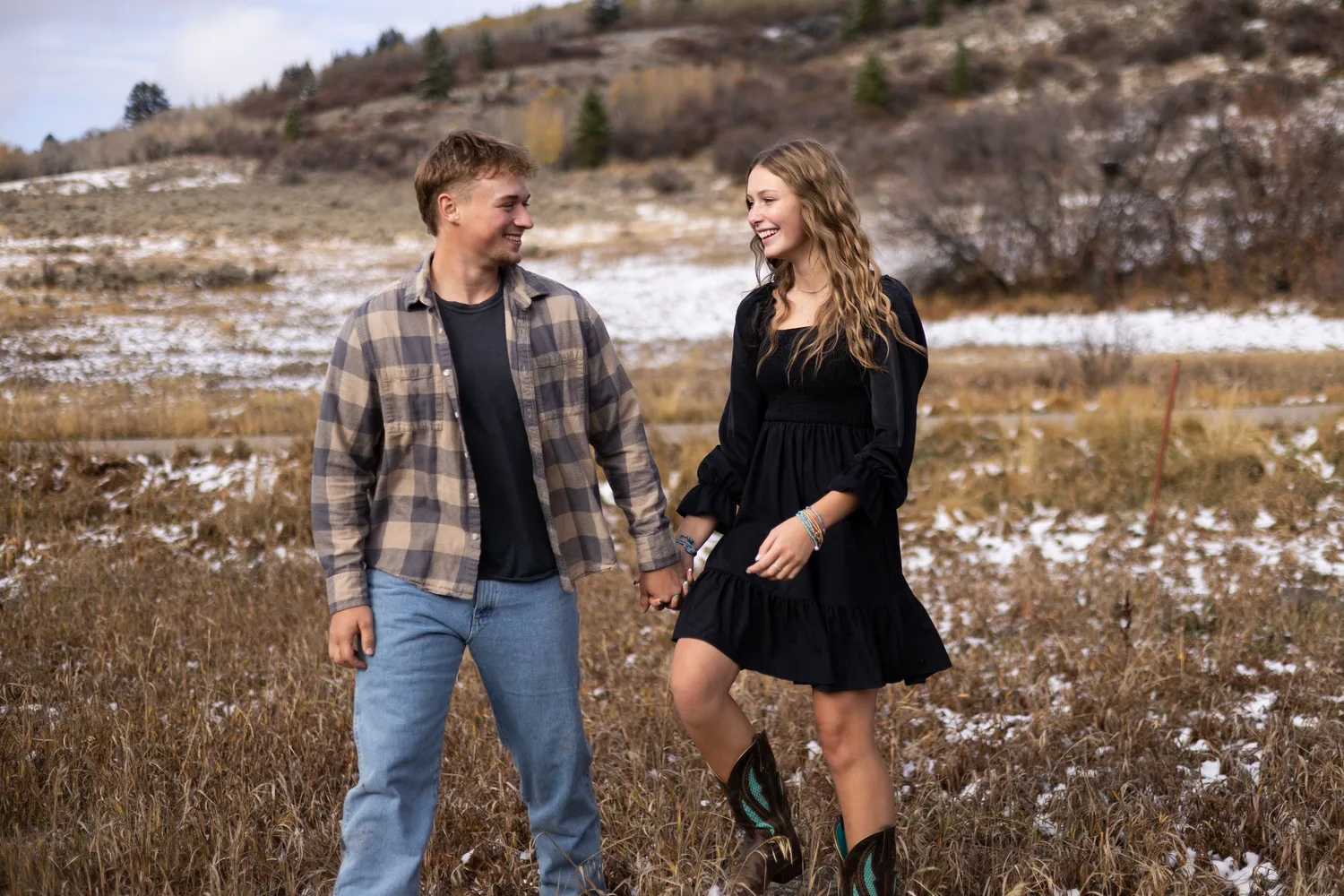 Couple in flannel and cowboy boots laughing in a snowy autumn field