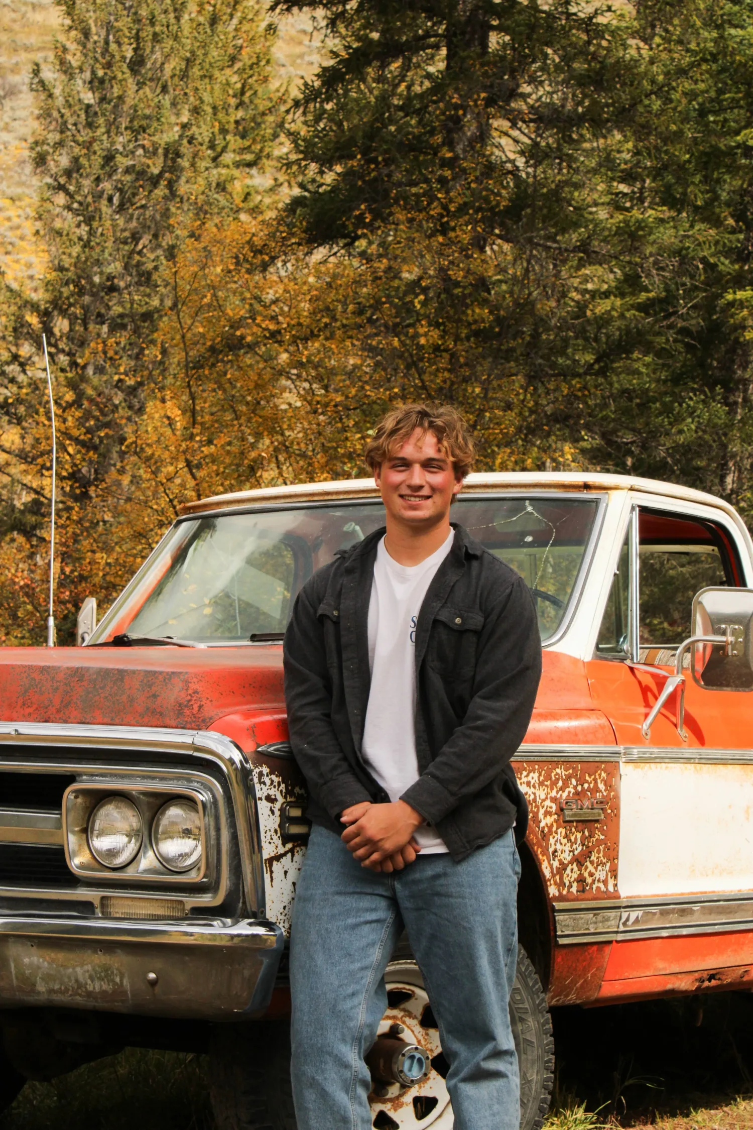 Senior portrait of a young man leaning on a vintage orange pickup in the woods