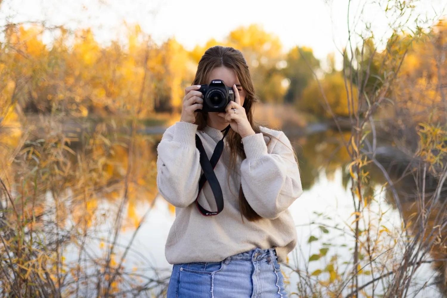 Toni Howell holding her camera up to her face beside an autumn pond