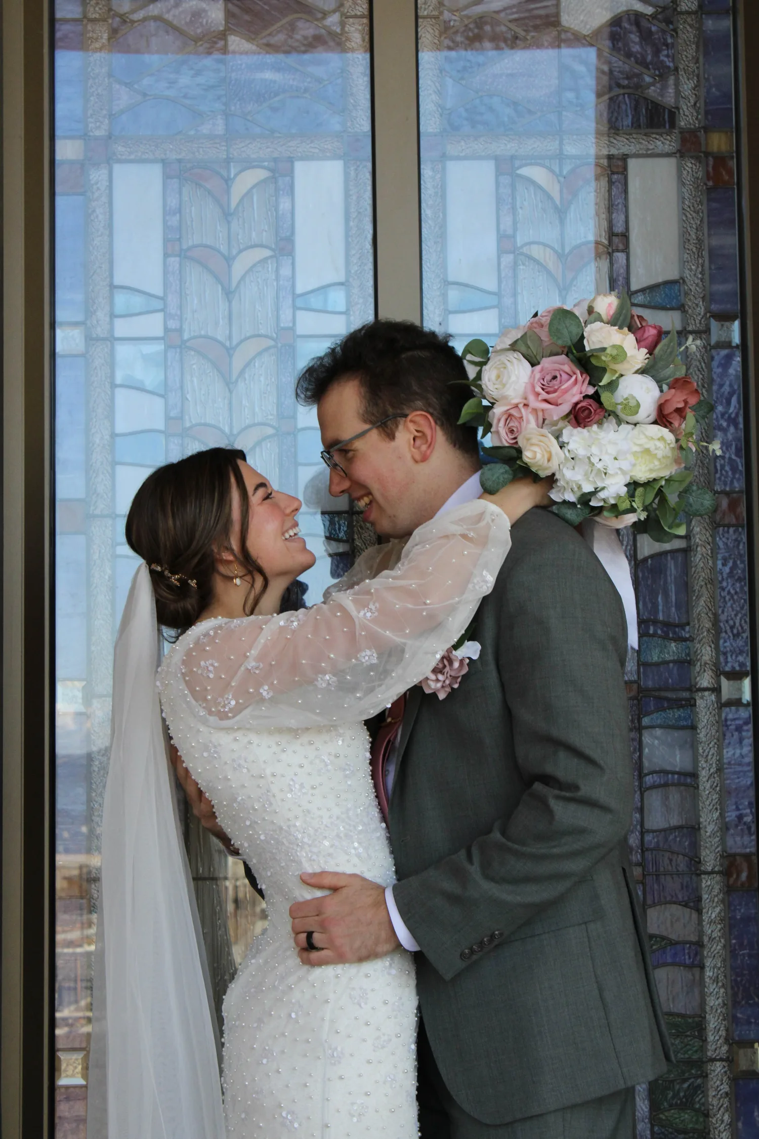 Bride and groom embracing in front of stained-glass windows