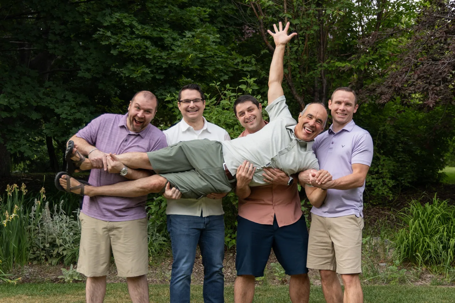Brothers playfully holding their friend sideways for a fun group photo