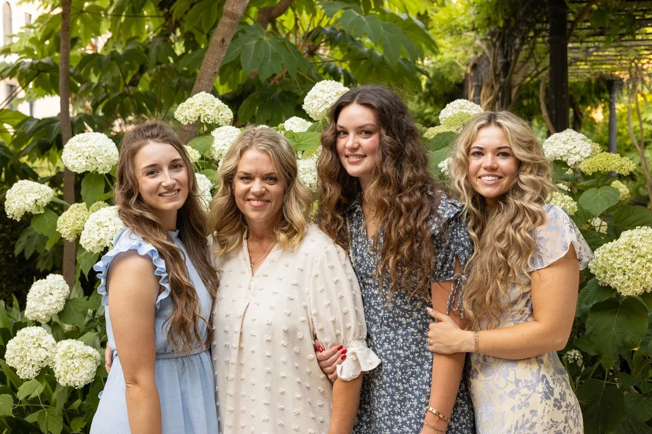 Mother and three daughters posing together in front of white hydrangeas