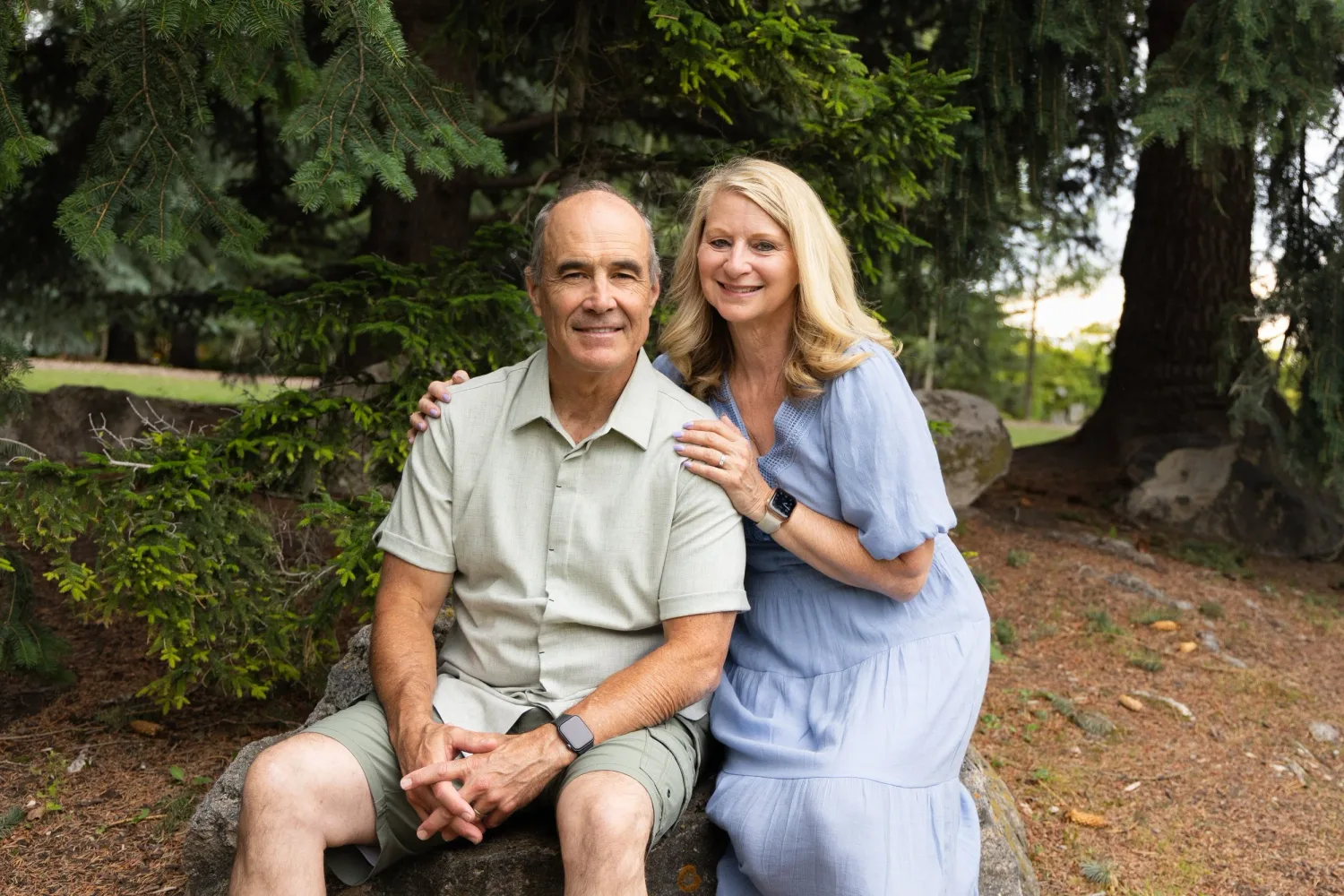 Older couple sitting together on a rock in a shaded wooded park