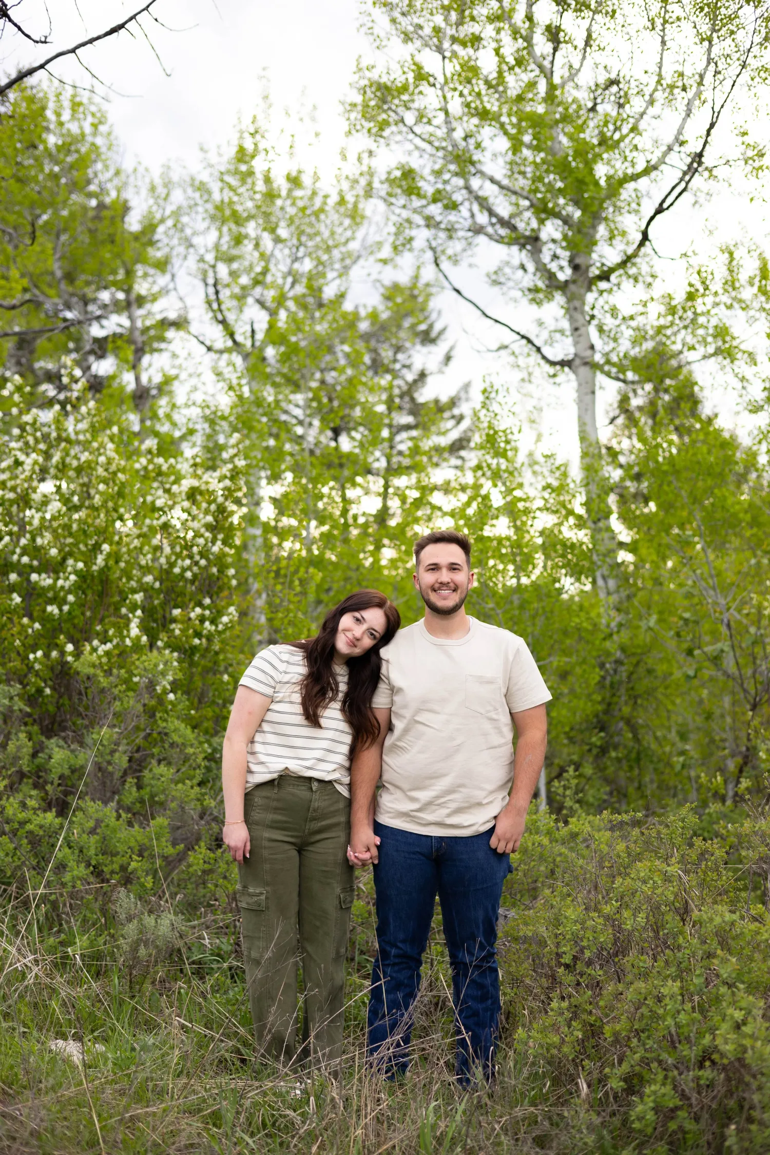 Couple standing together among green aspen trees in spring