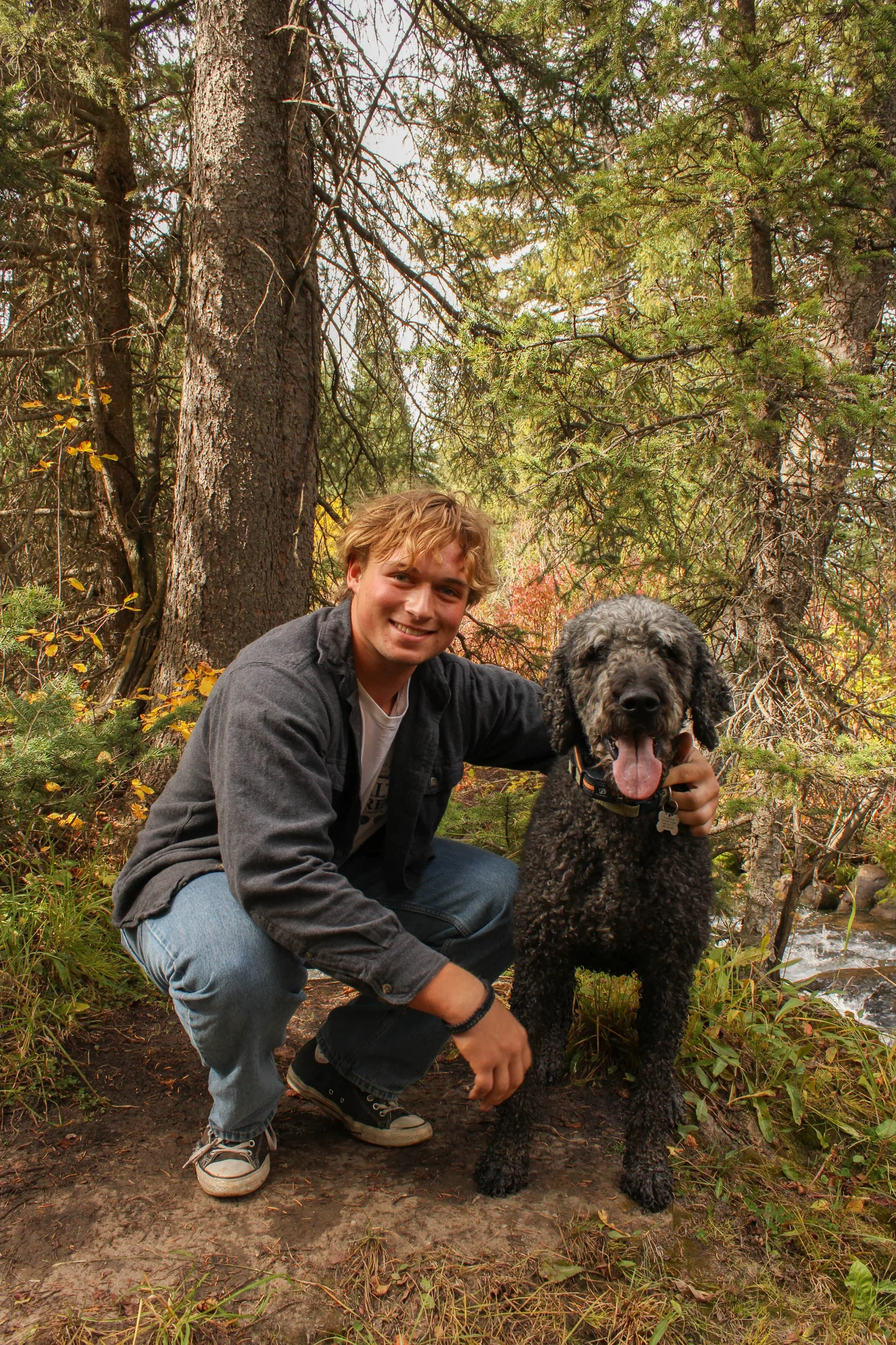Senior portrait of a young man crouching with his black dog in the woods