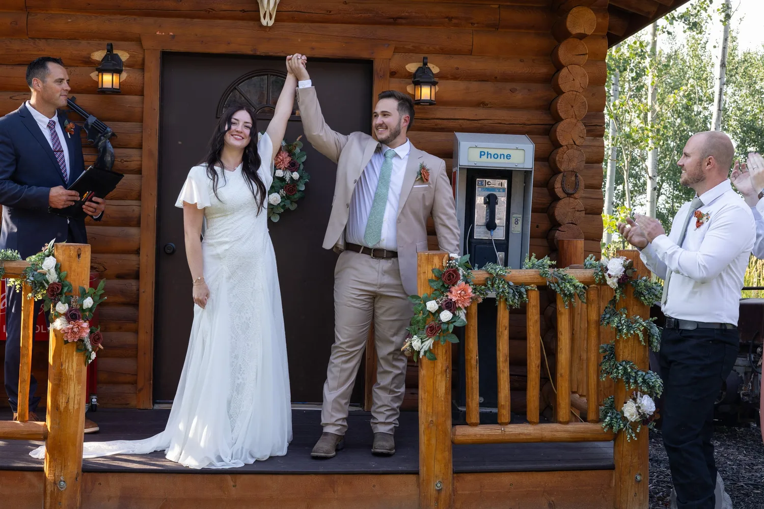 Bride and groom raising their joined hands after the ceremony on a log cabin porch