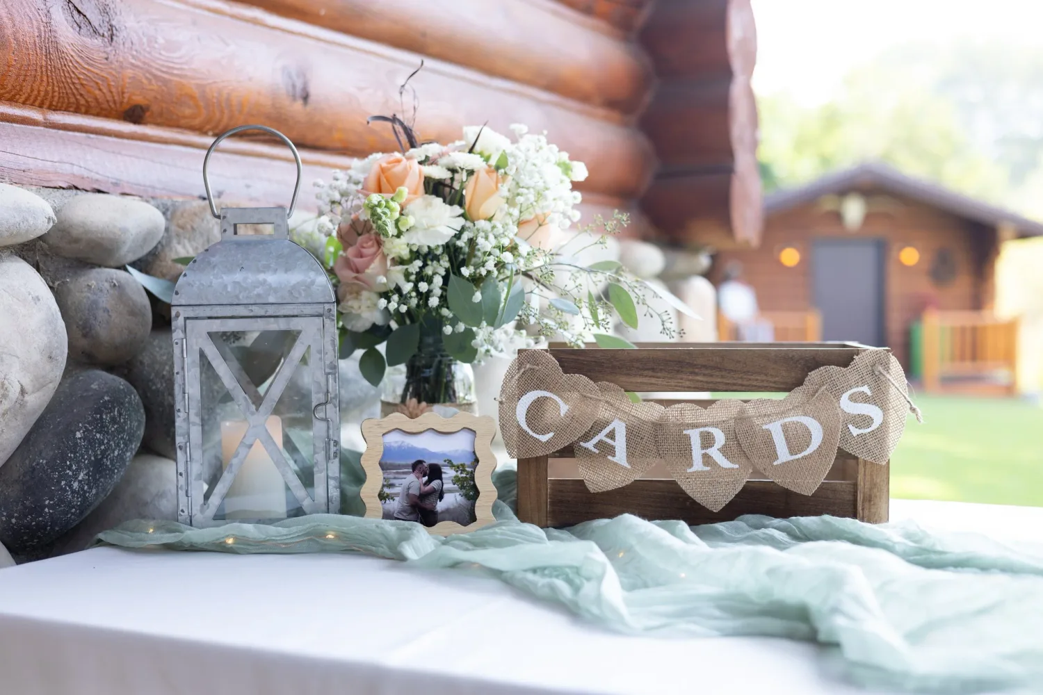Wedding card box, lantern and flowers on a table in front of a log cabin