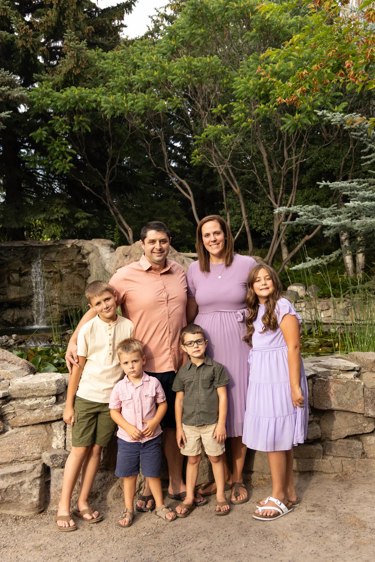 Family of seven posing in front of a rock waterfall feature in a garden