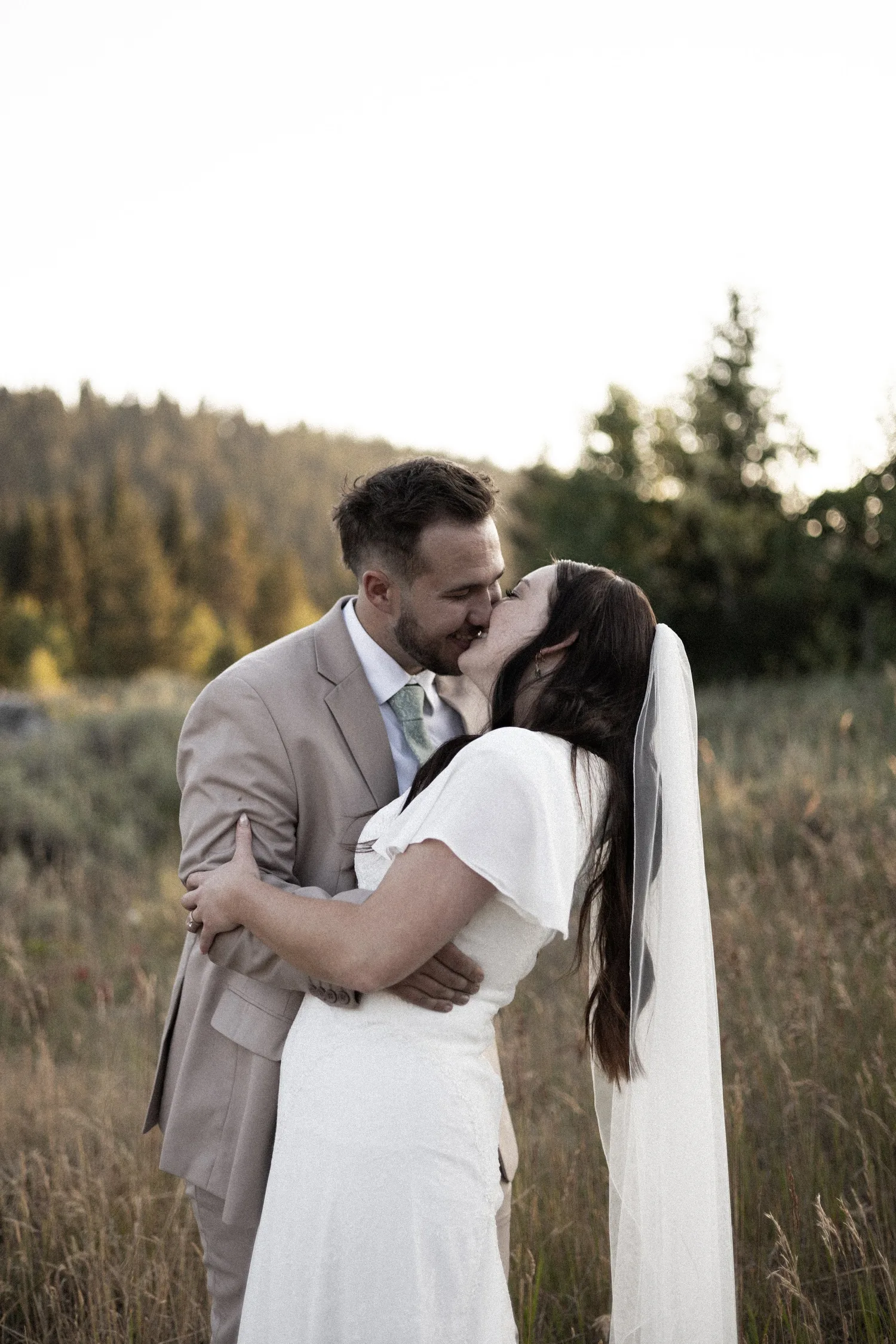 Bride and groom kissing in a sunlit mountain meadow