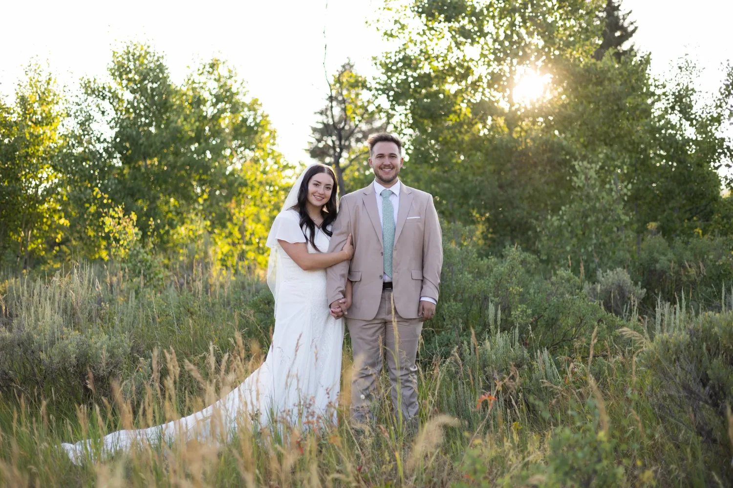 Bride and groom standing in tall grass at sunset