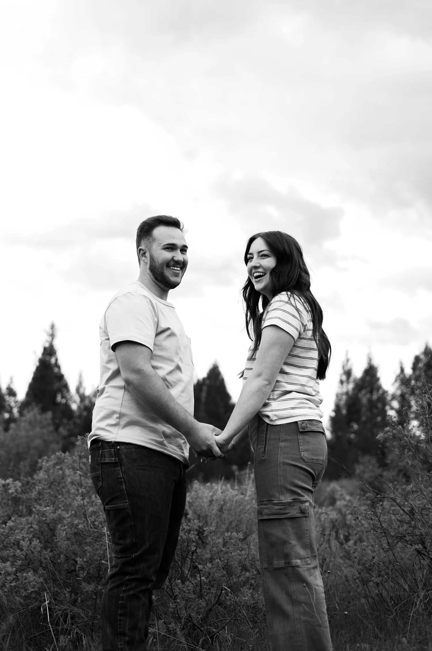 Black-and-white photo of a laughing couple holding hands in a meadow