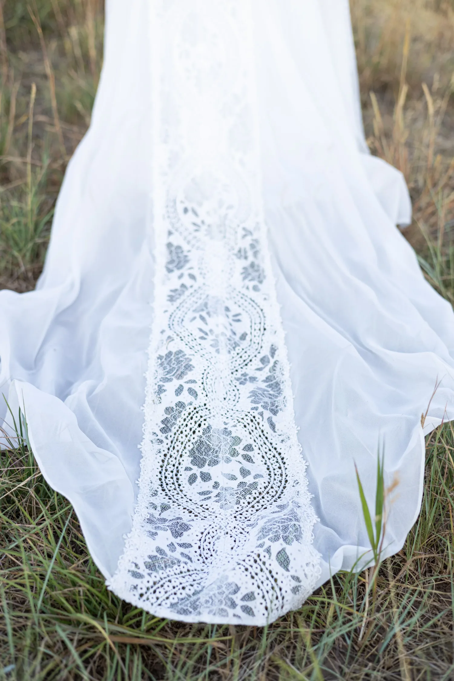 Close-up of the lace train of a wedding dress spread on the grass