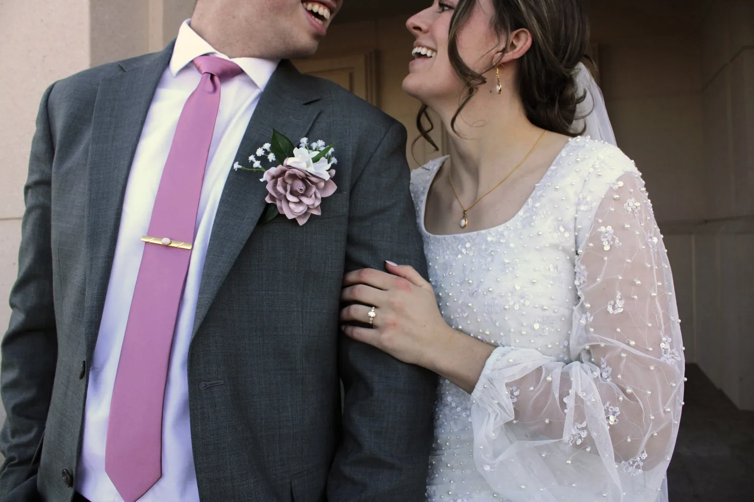 Close-up of a laughing bride and groom, groom wearing a pink tie and rose boutonniere