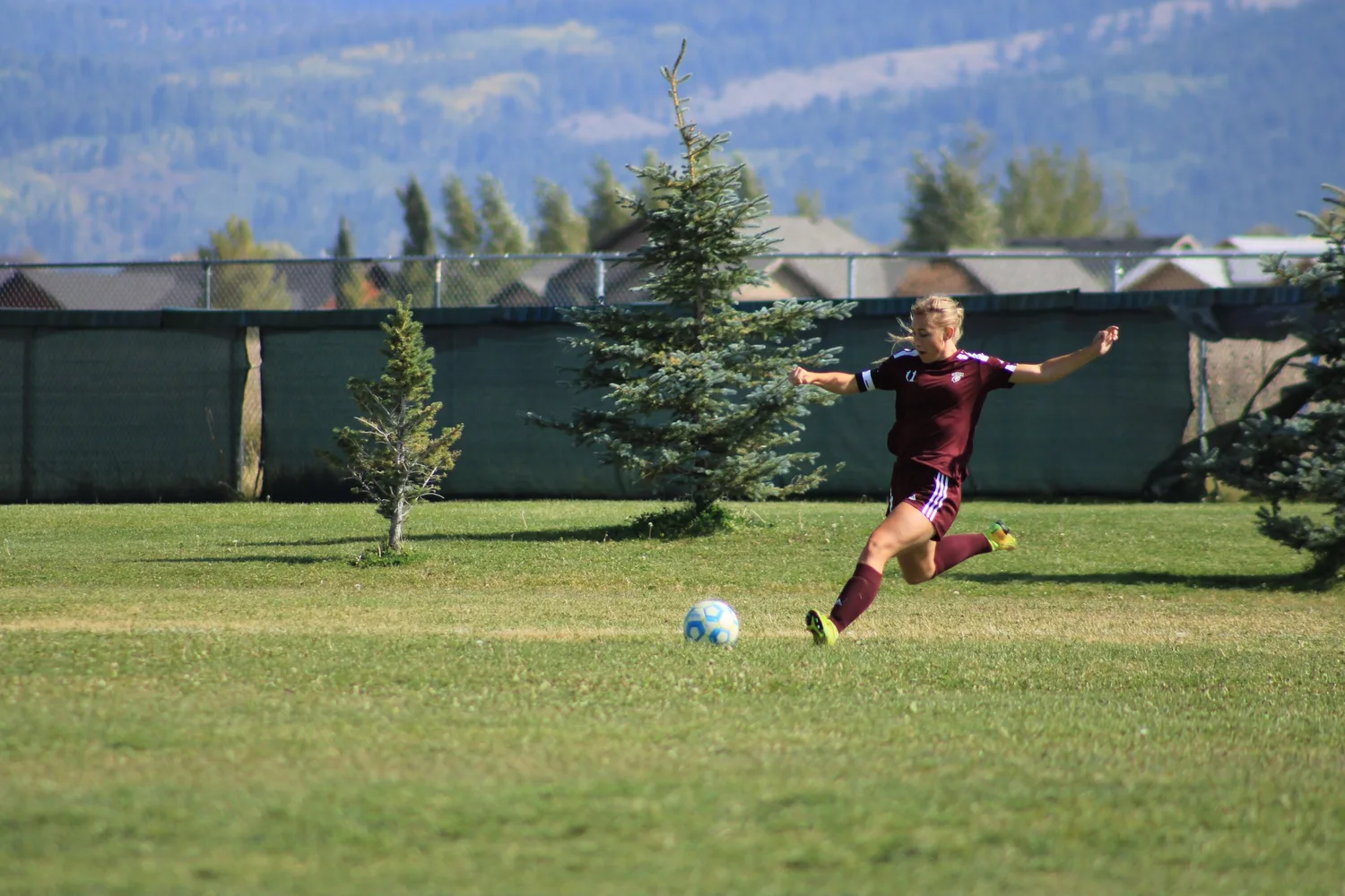 Soccer player taking a long kick on a field with mountains behind