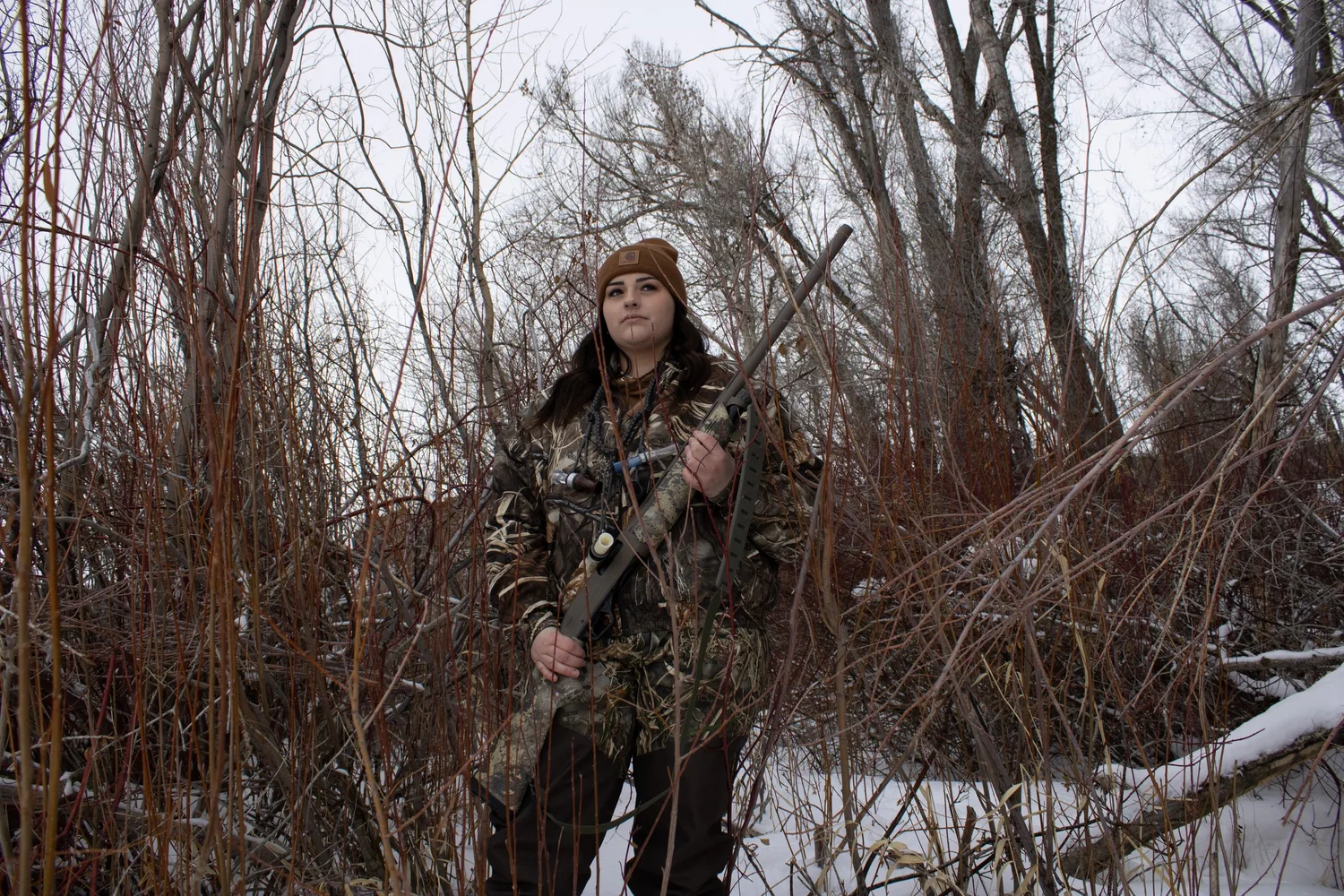 Hunter in camouflage holding a rifle among bare trees in the snow
