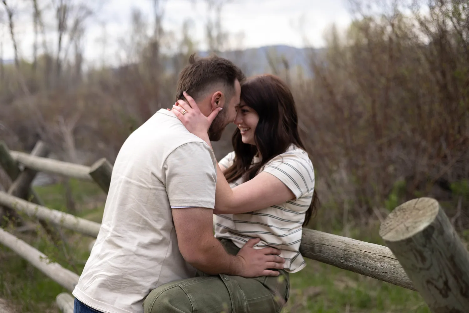 Couple leaning in close by a rustic wooden fence