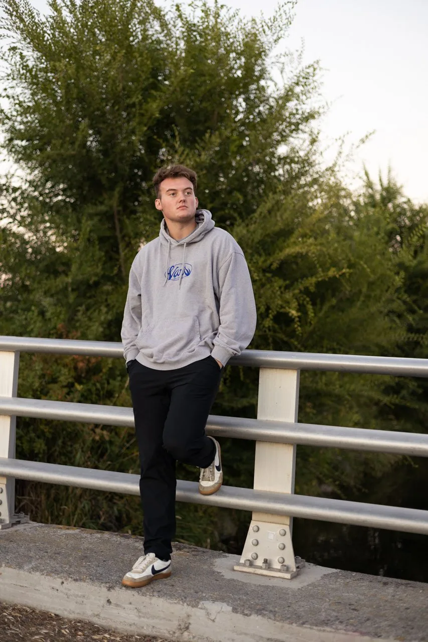 Senior portrait of a young man in a gray hoodie leaning on a bridge railing