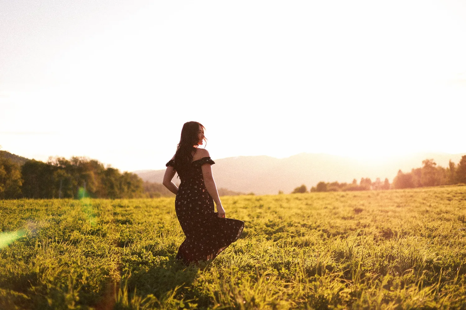 Silhouette of a woman in a dress walking through a meadow at sunset