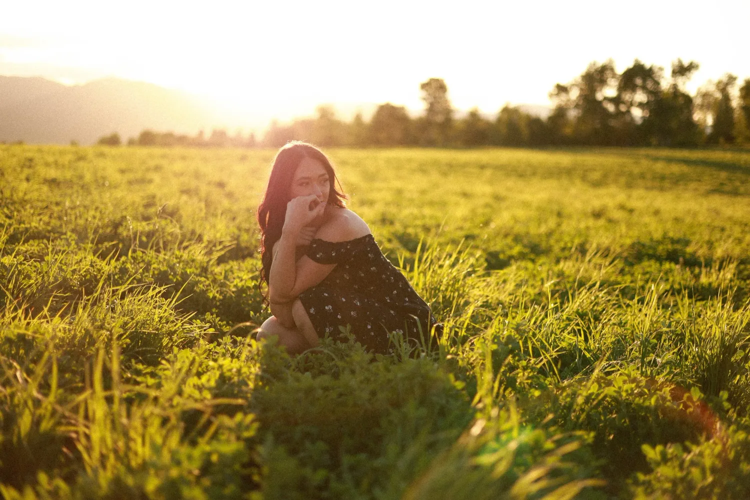 Young woman sitting in a sunlit green field at golden hour