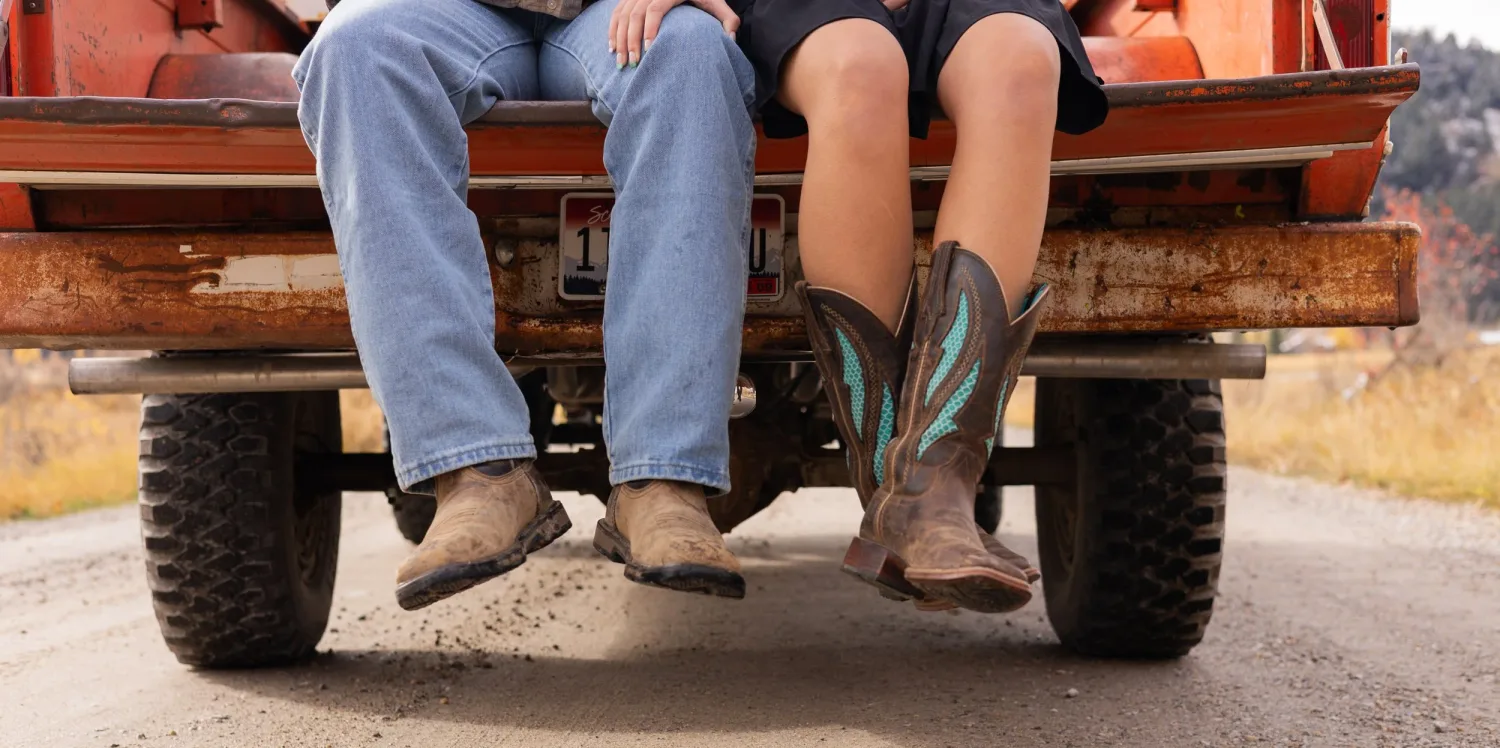 Close-up of a couple's boots dangling from an orange pickup tailgate