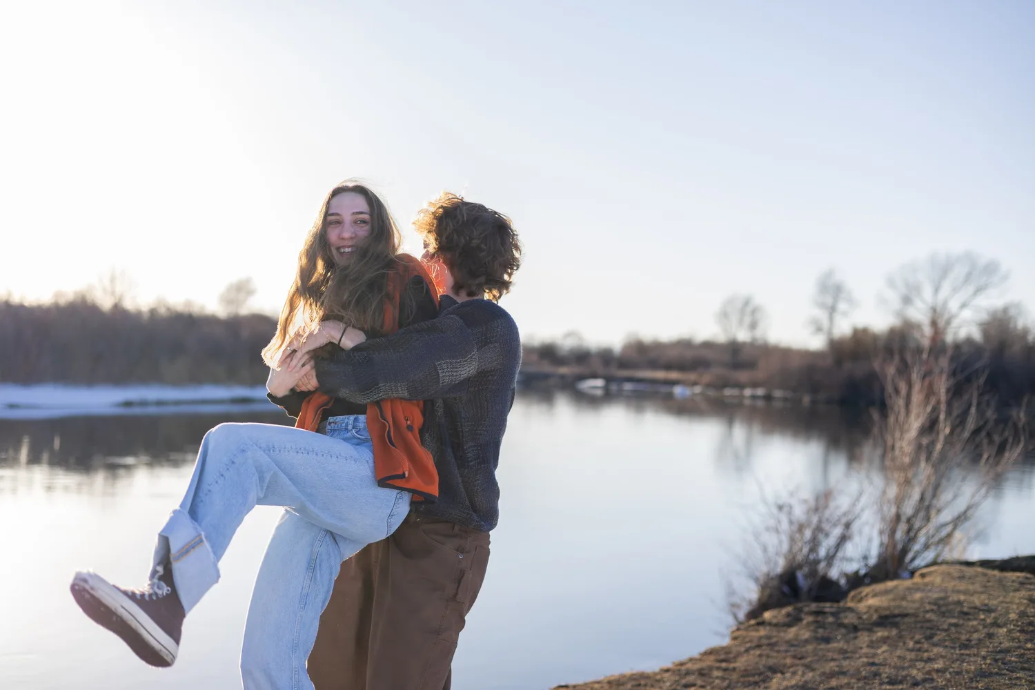 Man lifting his girlfriend off the ground beside a winter lake