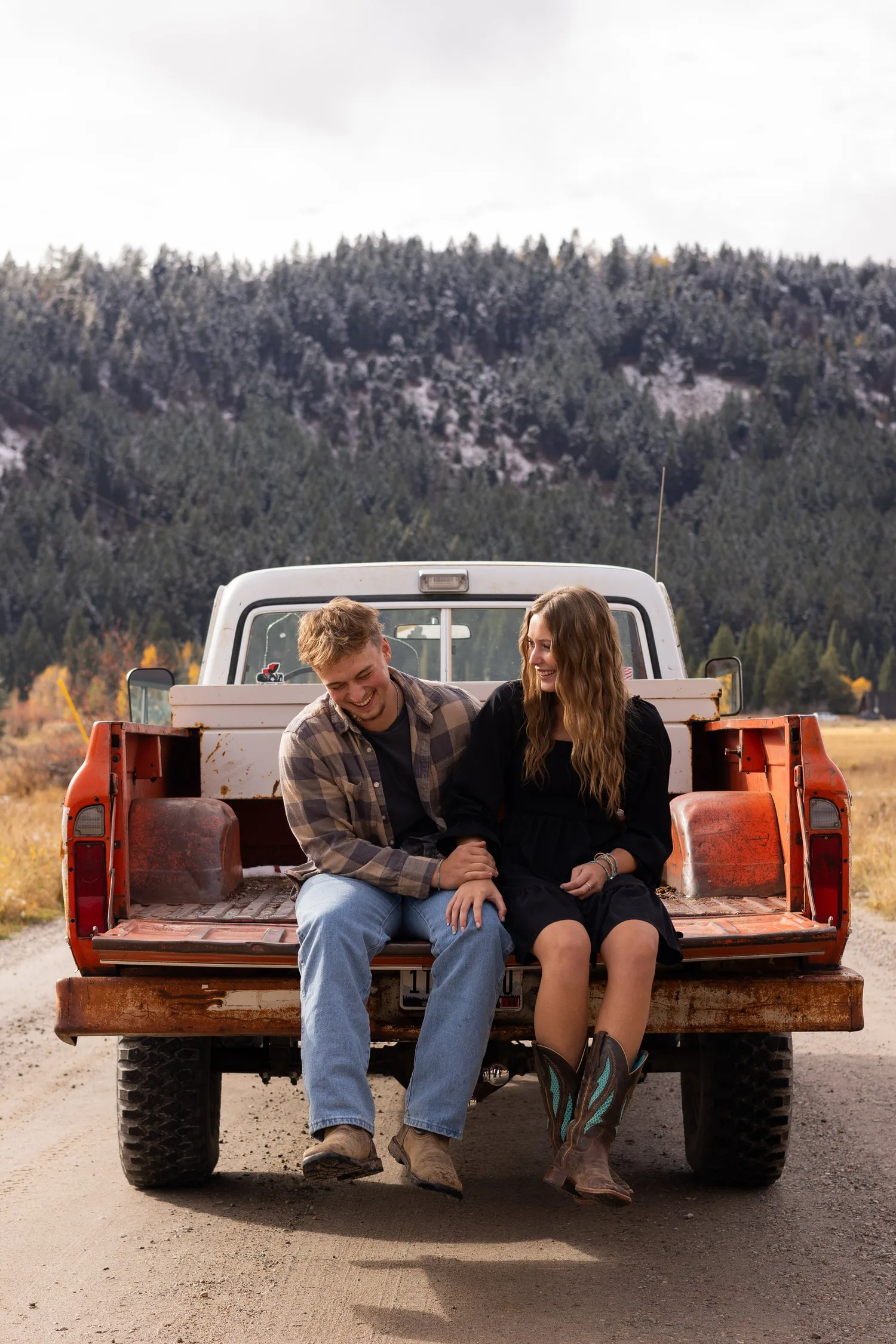 Couple sitting on the tailgate of an orange vintage pickup on a mountain road